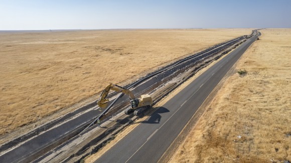 Yellow excavator digging in a dirt trench