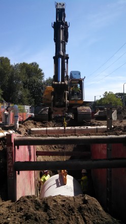 IMCO REDMOND workers and excavator at construction site with large pipe under dirt