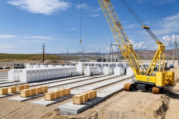 Yellow crane hoisting batteries for renewable energy at power storage project.
