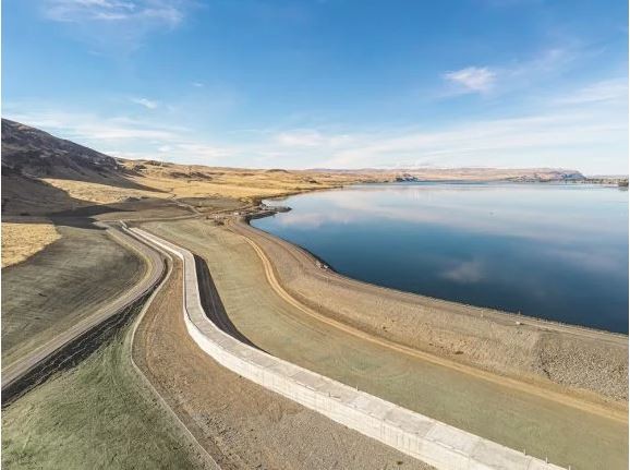 Concrete dam surrounded by blue water and brown hills 