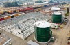 Two large green round metal tanks in front of steel framing and train cars