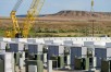 Yellow crane hoisting batteries at energy storage site, renewable energy