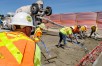 Construction workers in hard hats and high visibility vests working on I-90 roadway to place concrete during a closure, with blue sky in background