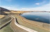 Concrete dam surrounded by blue water and brown hills 