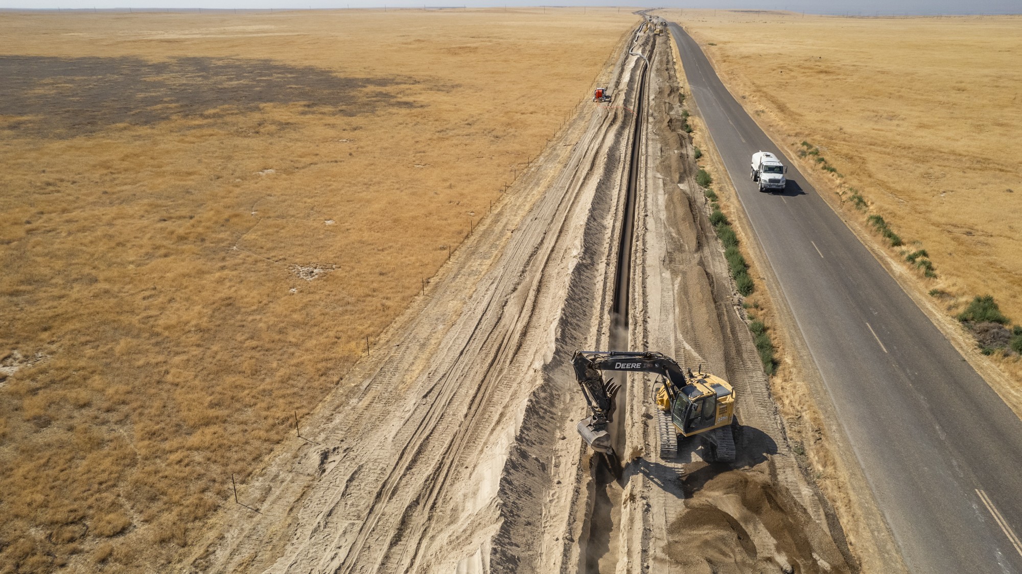 Yellow excavator laying black pipe in dirt trench