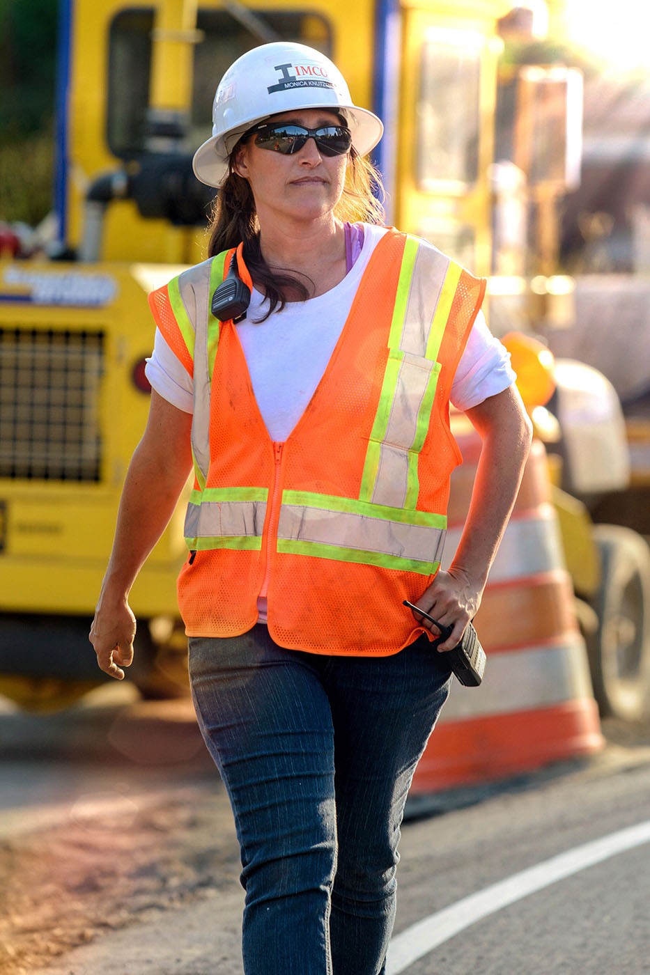 Woman walking across construction site with hardhat, orange vest and relentless safety text