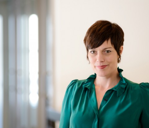 Ashley Kimberley standing in natural light in office, wearing emrald green blouse.