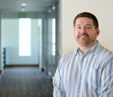 Jim Cooper standing in natural sunlight in office building, wearing striped shirt