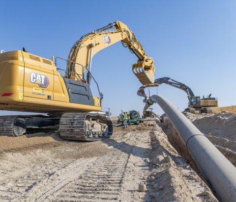 Yellow tractor placing pipe in dirt field under blue sky