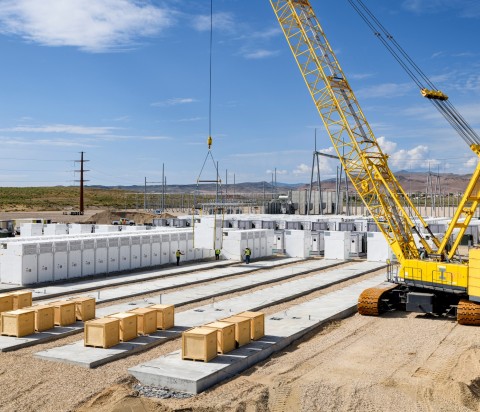Yellow crane hoisting batteries for renewable energy at power storage project.