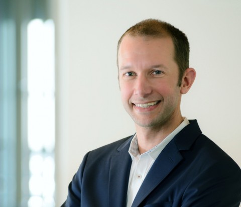 Tyler Kimberley, wearing white shirt and navy blazer, standing with arms crossed with natural sunlight