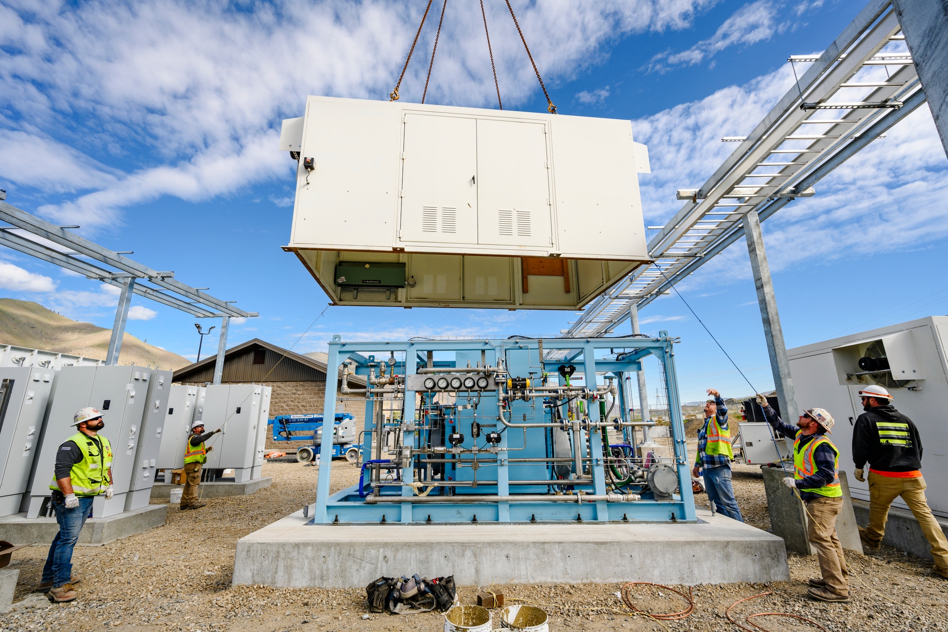 men working on construction site, guiding large equipment on cables to concrete slab