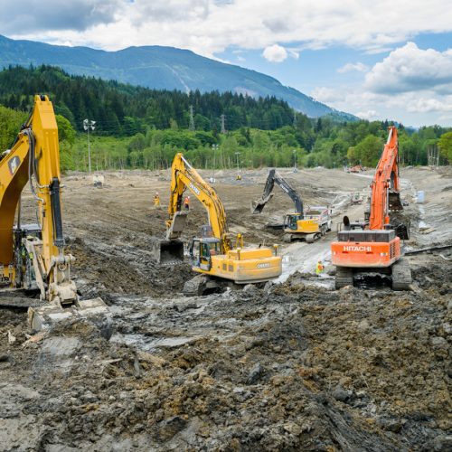 Group of excavators working in the mud with mountain in background