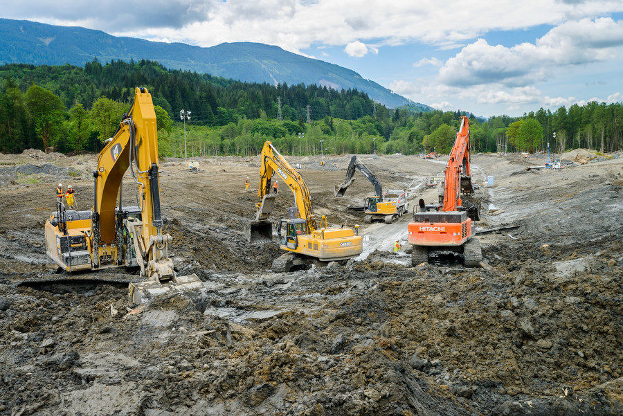 Group of excavators working in the mud with mountain in background