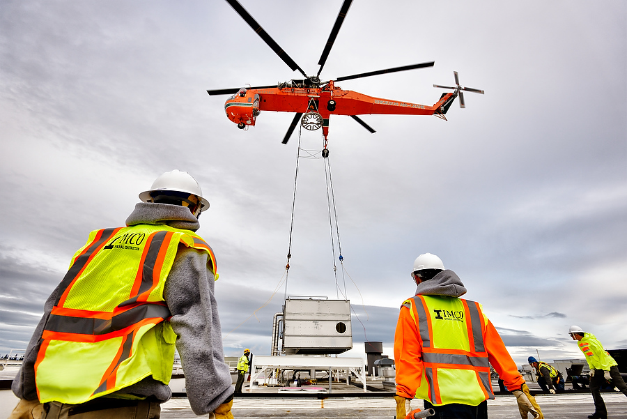 people in hard hats and vests looking up at helicopter setting equipment on building