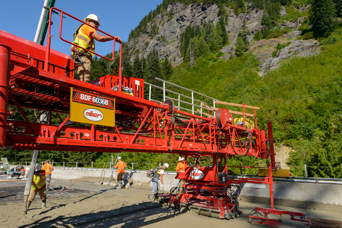 red heavy machinery with people working along roadway and mountain in background