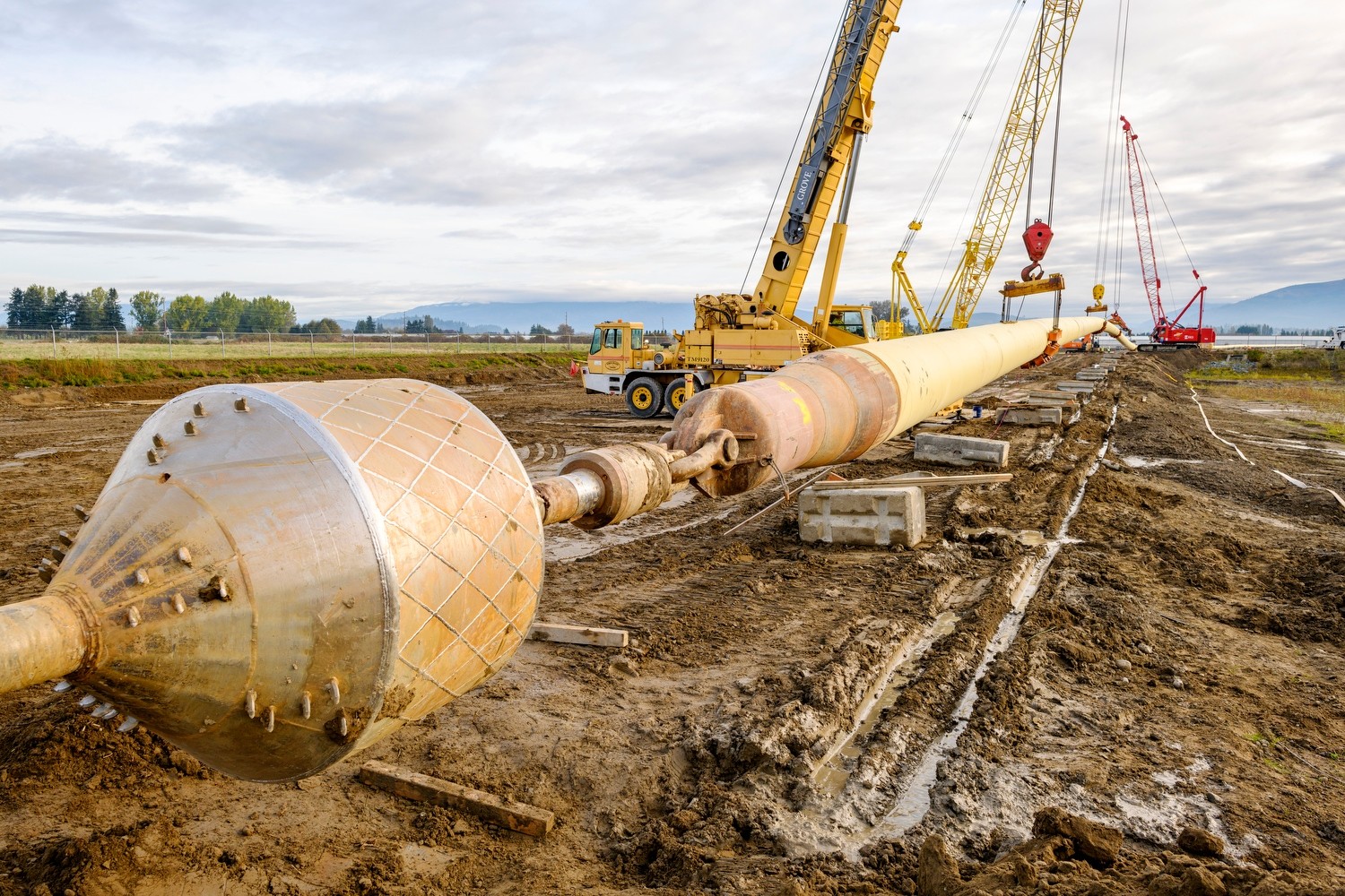 Skagit raw water project landscape Construction site with large pipeline, red crane, yellow crane, excavator, and truck in mud