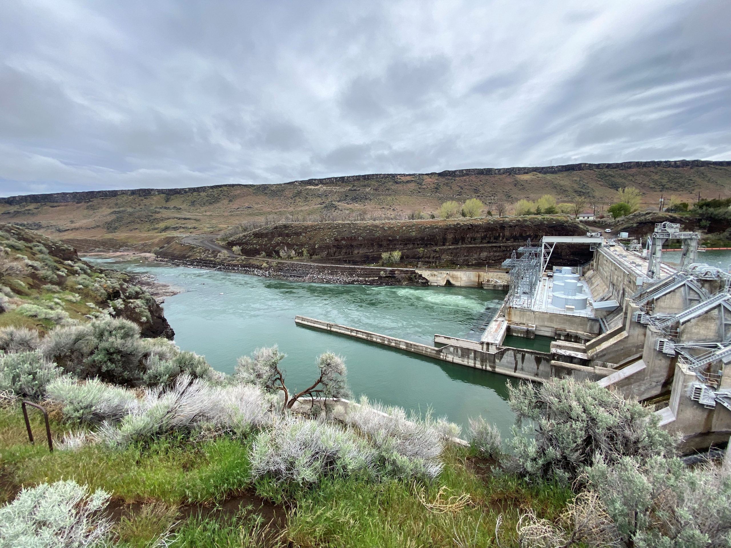 dam on green water surrounded by dirt landscape