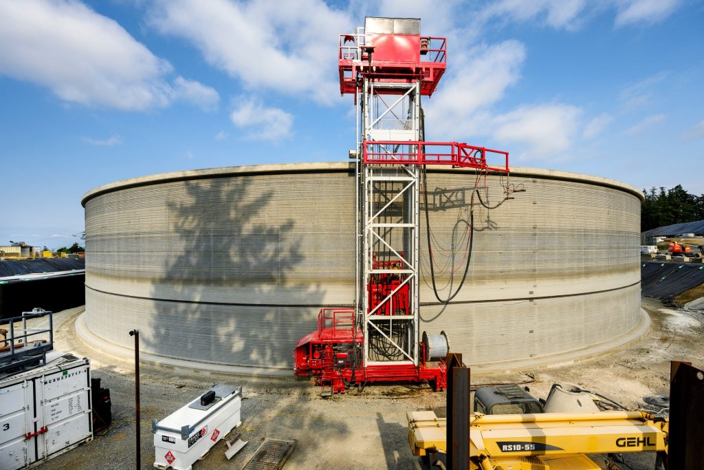 Round concrete tank with red scaffolding machine under a blue sky.