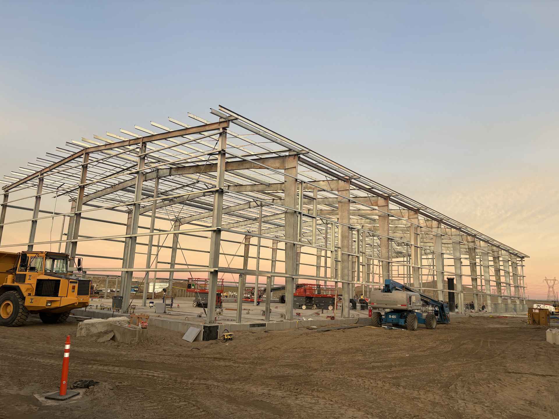 Metal framed building on dirt site surrounded by construction vehicles
