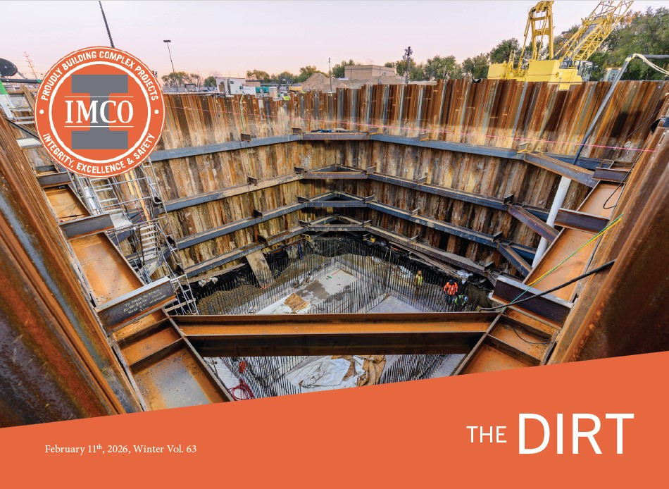 A large open pit being constructed with a man working in it. The pit is surrounded by metal framing and there is a crane in the background.