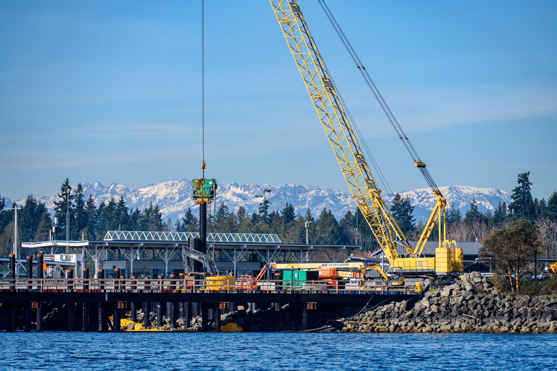 water foreground, mountains in background, yellow construction crane along pier adjacent to ferry terminal